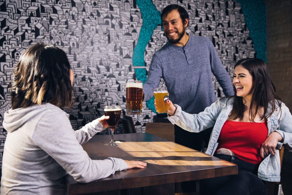 Gruppe voksne sitter rundt bordet i en urban bar og skåler med glass i god stemning