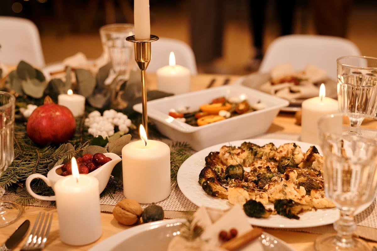Festlig dekket langbord til julebord med levende lys, glass og vintergrønn pynt i varm belysning