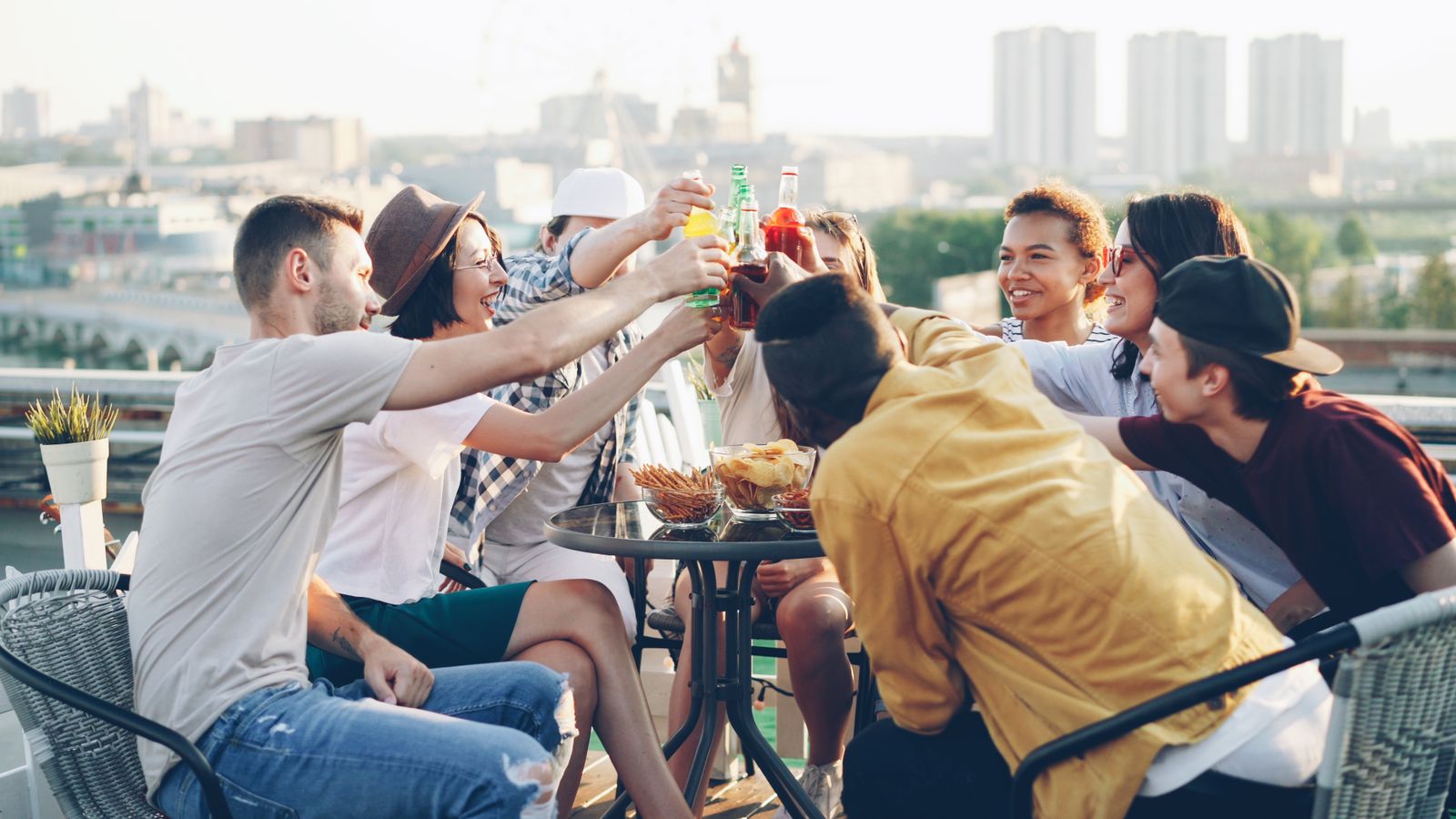Venner som skåler med drinker på en takterrasse i solnedgang
