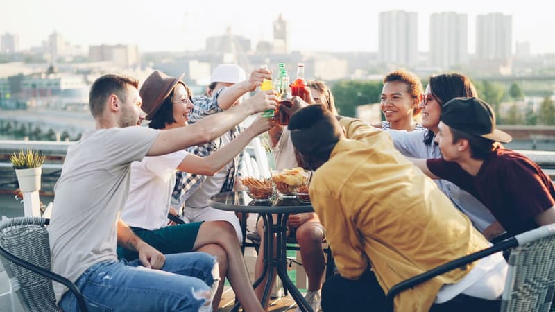 Venner som skåler med drinker på en takterrasse i solnedgang