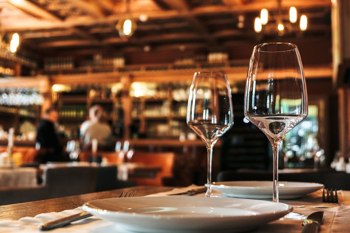 Nærbilde av dekket restaurantbord med vinglass, bestikk og servietter i varm, dempet belysning